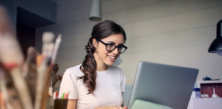 woman with glasses typing college admissions essay on laptop