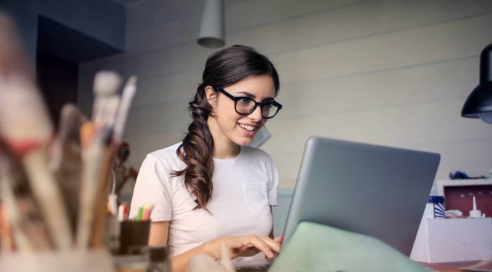 woman with glasses typing college admissions essay on laptop