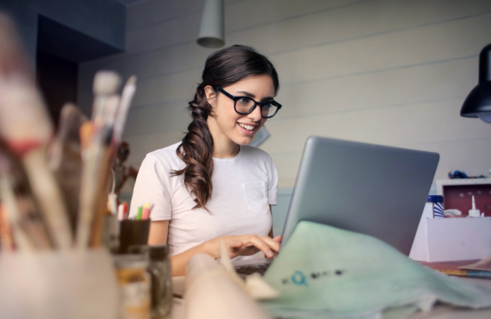 woman with glasses typing college admissions essay on laptop