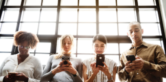 women and men holding smart phone in front of window