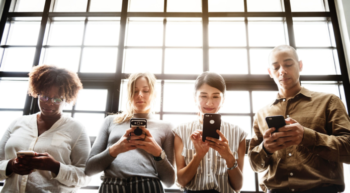 women and men holding smart phone in front of window