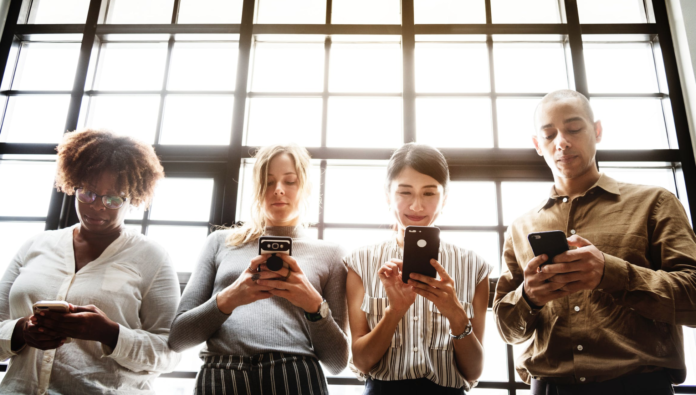 women and men holding smart phone in front of window