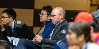 man with bald head and glasses sits in college room