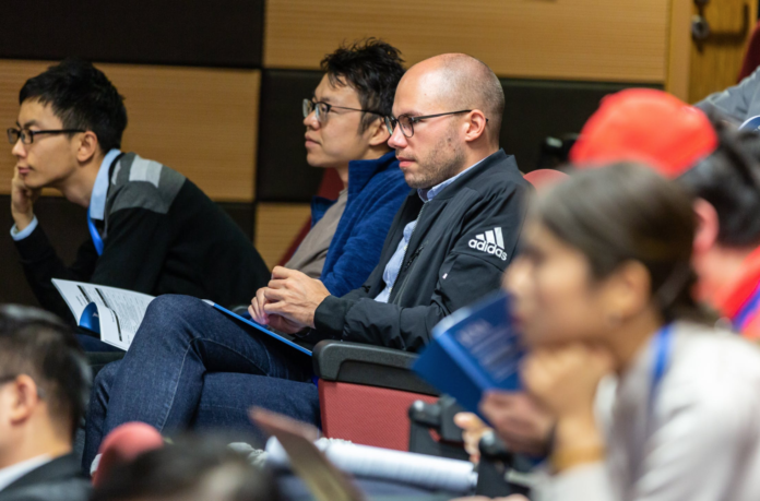 man with bald head and glasses sits in college room