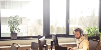 man in office inn front of window working on laptop wearing headphones