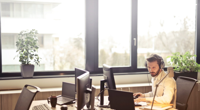 man in office inn front of window working on laptop wearing headphones