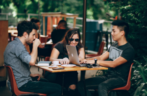 three people sitting a table working on their labtops 