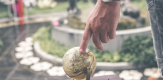 man pointing at little globe on wood table