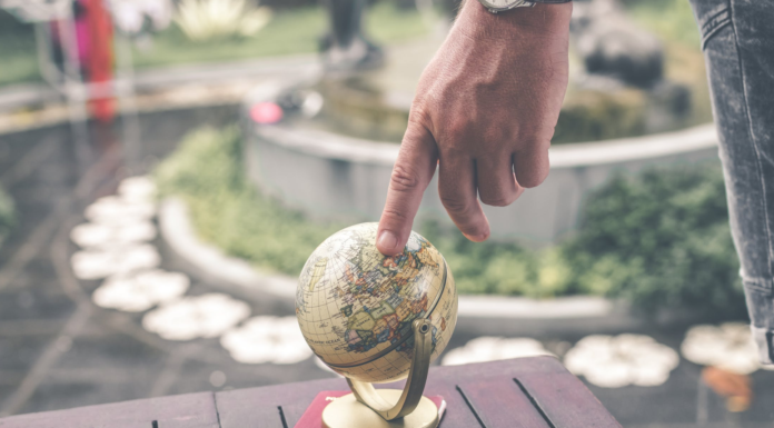 man pointing at little globe on wood table